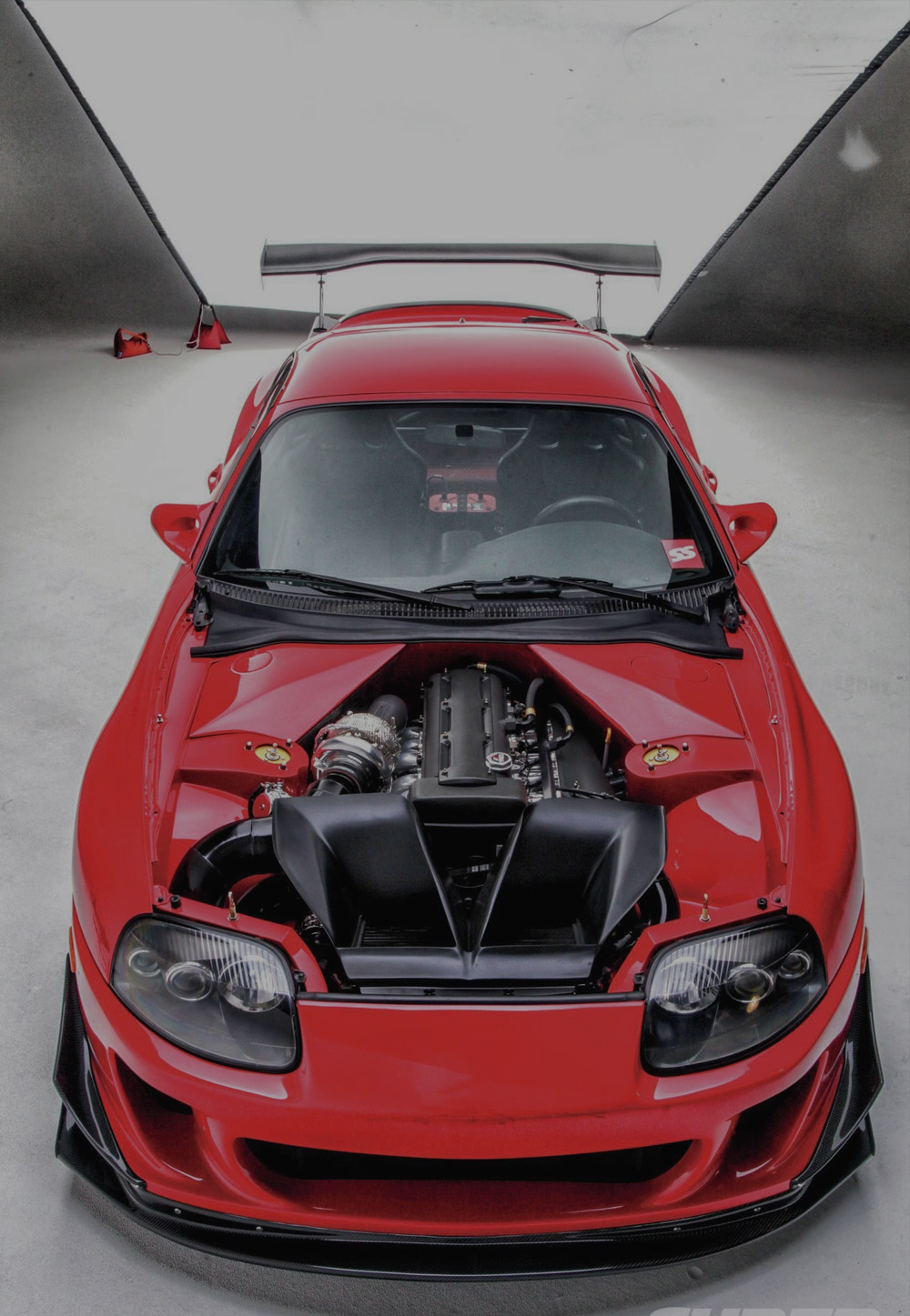 A red performance car photographed from above with the engine bay visible